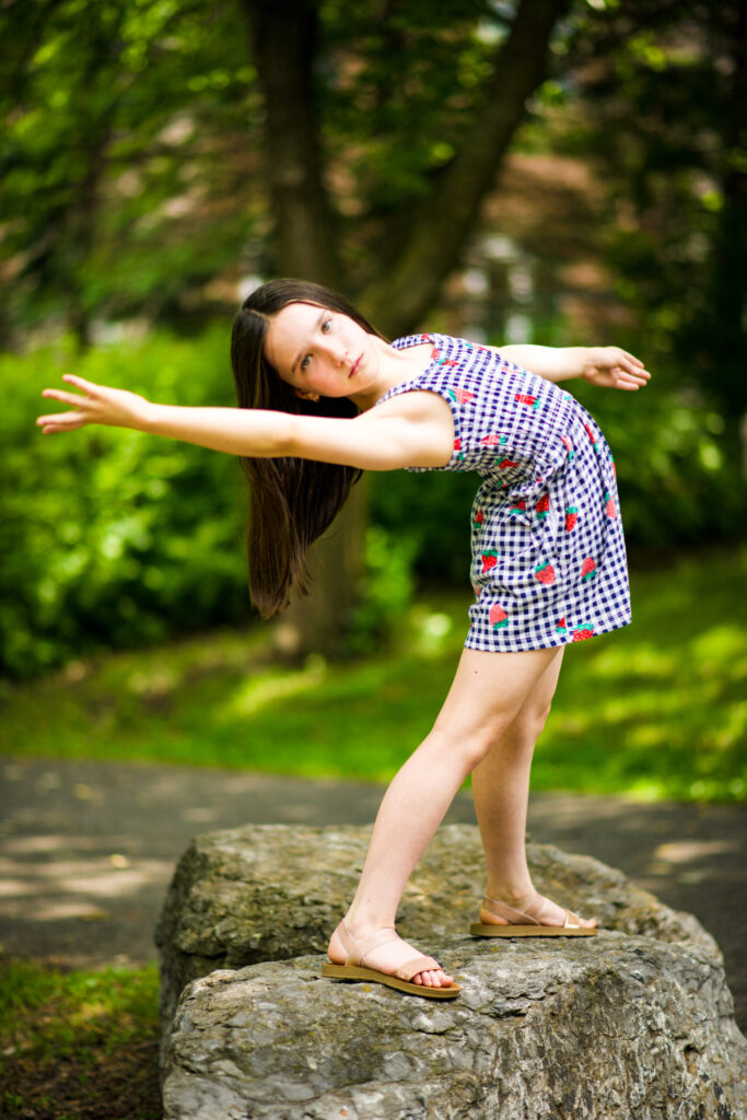 Young dancer standing outdoors on a rock in a dramatic backbend pose